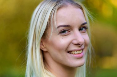 Güzel sarışın kız parkta sonbahar günbatımı güneş akşam sokakta fotoğraf portre. Gülümseyen ve mutlu görünüyordu kamera önünde duruyor.