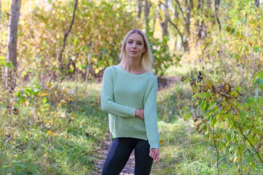 Güzel sarışın kız ormanda niteliğine parkta fotoğraf portre. Gülümseyen ve mutlu görünüyordu şu kamera önünde duruyor.