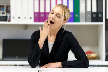 Studio fotoğraf güzel bir sarışın kız bir masada oturan bir ofiste iş takım elbiseli konuşuyor. Gülümseyen ve mutlu görünüyordu şu kamera önünde oturuyor.