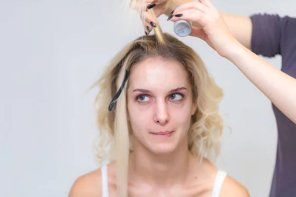 The work of a professional makeup artist - hairdresser, makes the hair style of a beautiful blonde girl. The model is right in front of the camera.