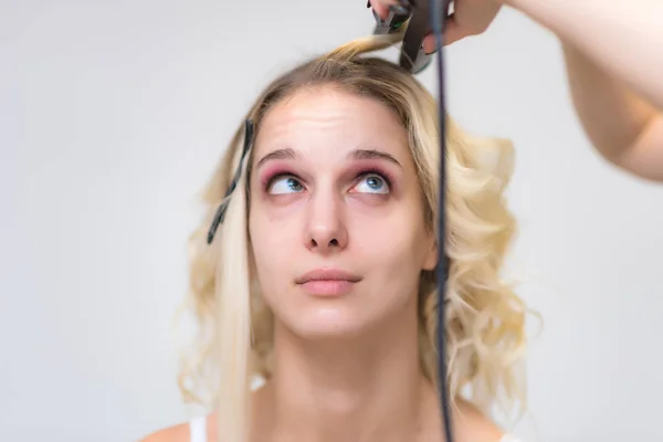 The work of a professional makeup artist - hairdresser, makes the hair style of a beautiful blonde girl. The model is right in front of the camera.