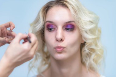 İş bir profesyonel makyaj sanatçısı - güzellik uzmanı, gölgeler modelinin göze güzel bir sarışınla yüzünde bir fırçayla makyaj yapar. Kaş boyama.