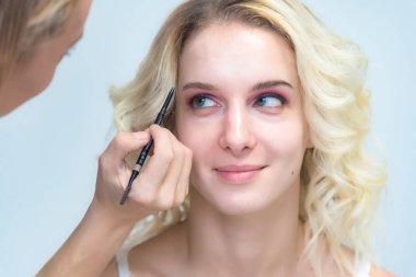 İş bir profesyonel makyaj sanatçısı - güzellik uzmanı, gölgeler modelinin göze güzel bir sarışınla yüzünde bir fırçayla makyaj yapar. Kaş boyama.