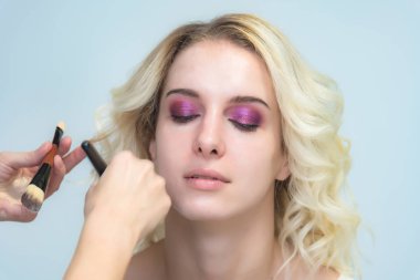 İş bir profesyonel makyaj sanatçısı - güzellik uzmanı, gölgeler modelinin göze güzel bir sarışınla yüzünde bir fırçayla makyaj yapar. Kaş boyama.