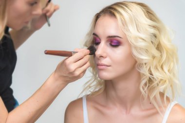 İş bir profesyonel makyaj sanatçısı - güzellik uzmanı, gölgeler modelinin göze güzel bir sarışınla yüzünde bir fırçayla makyaj yapar. Kaş boyama.