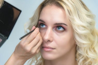 İş bir profesyonel makyaj sanatçısı - güzellik uzmanı, gölgeler modelinin göze güzel bir sarışınla yüzünde bir fırçayla makyaj yapar. Kaş boyama.