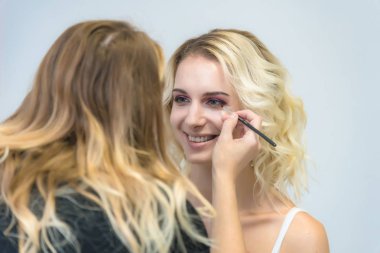 İş bir profesyonel makyaj sanatçısı - güzellik uzmanı, gölgeler modelinin göze güzel bir sarışınla yüzünde bir fırçayla makyaj yapar. Kaş boyama.