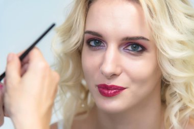 İş bir profesyonel makyaj sanatçısı - güzellik uzmanı, yapar makyaj fırçasıyla yüzünde güzel bir sarışın manken dudaklarından. Güzel makyaj için sarışın model oluşturma makyaj sanatçısı