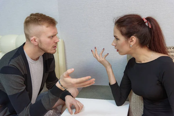 The concept of family conflict, family problems, family relationships of young disgruntled husband and wife in a room on the sofa. They sit across from each other and look displeased.