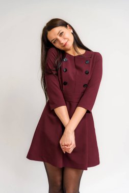 Stüdyo bir elbise beyaz bir arka plan üzerinde güzel bir esmer kız portresi. Gülümseyen ve mutlu görünüyordu şu kamera önünde duruyor.