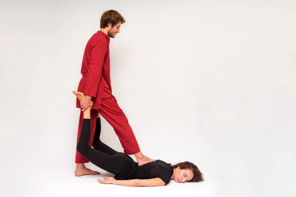 Photo of yoga poses on the floor for two stretching and relaxing on a white background. The man stretches the woman right in front of the camera.