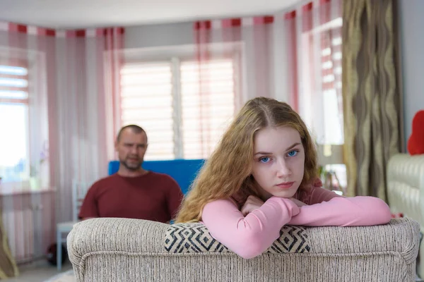 Family problems, family relations father and teen daughter in a room on the sofa. They are sitting right in front of the camera, arguing and looking displeased.