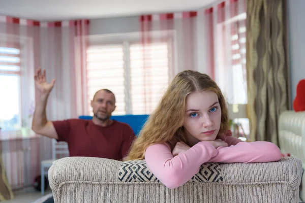 Family problems, family relations father and teen daughter in a room on the sofa. They are sitting right in front of the camera, arguing and looking displeased.