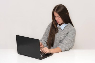 Güzel bir genç kız ile bir dizüstü bilgisayar bir masada oturan beyaz bir arka plan üzerinde portresi. O kamera önünde farklı duygular ile çeşitli teşkil etmektedir haklı.