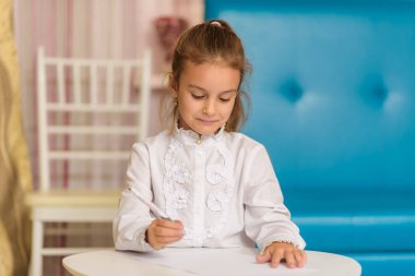 Sevimli küçük bir kız çizim ve bir şey söylüyor bir masada oturuyor. Çocuk şu kamera gülümseyen önünde ve mutlu görünüyor.