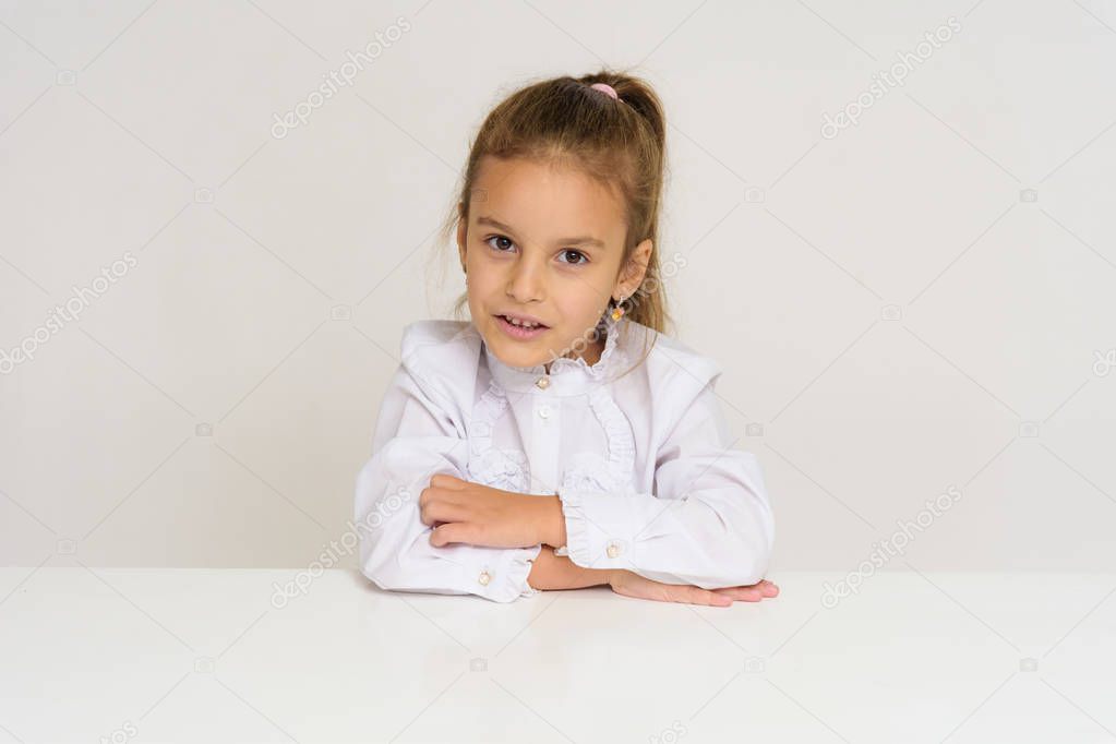 Portrait of a cute baby girl on a white background at the table. The child is right in front of the camera, smiling and looking happy