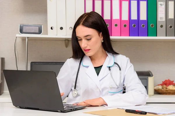 Portrait of a brunette doctor in the office at the table. The doctor sits right in front of the camera and talks to the patient