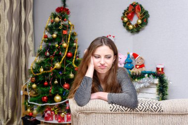 Bir parlak zarif gece elbisesi, yeni yıl arifesinde Noel ağacı ve hediyeler yakınında oturan genç güzel kadın. İç Noel dekorasyonu ile. Kamera önünde.