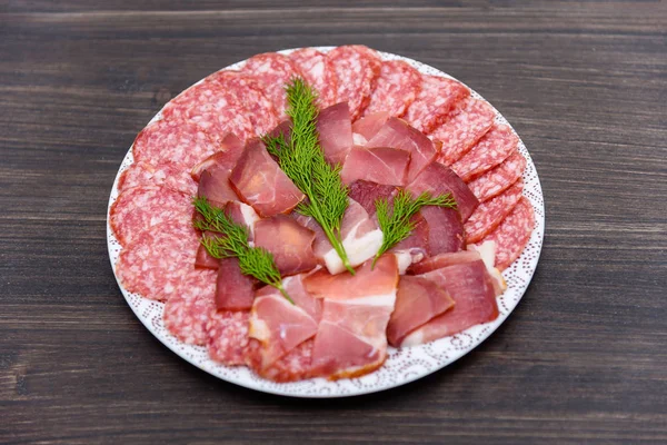 Food tray with delicious salami, pieces of sliced ham, sausage, tomatoes, salad and vegetable. Cutting sausage and cured meat on a celebratory table. Meat platter with selection.