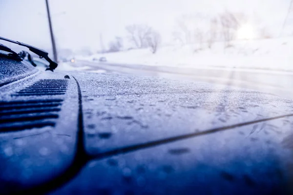 Rear view mirror on a snow-covered car, standing in the Parking lot near the house on a cold morning, the sun shines into the camera. Closeup of car tires in winter on the road covered with snow.