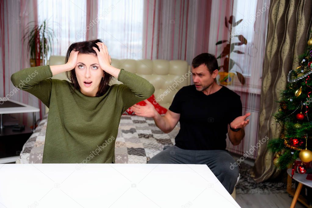 The concept of the wife sits by the table with the husband in the room against the window and argue. they are in the middle of the photo and talk about something.