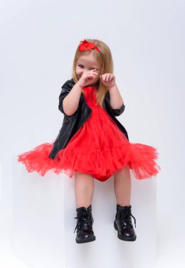 Şirin güzel bir kız bebek beyaz bir arka planda bir moda kırmızı elbiseli kavramı portresi. O kameranın çeşitli teşkil etmektedir küp önünde oturur ve farklı duygular gösterir.