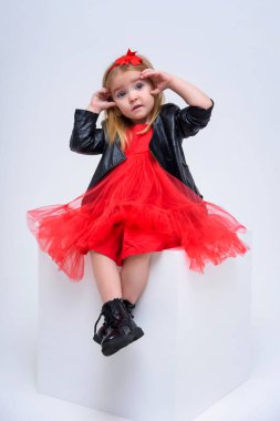 Şirin güzel bir kız bebek beyaz bir arka planda bir moda kırmızı elbiseli kavramı portresi. O kameranın çeşitli teşkil etmektedir küp önünde oturur ve farklı duygular gösterir.