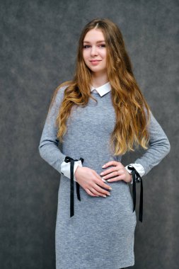 Mutlu brunet kız güzel uzun saçlı hoş bir dostu Müdürü kavramı portresi. Tam büyüme gri bir arka plan karşı gülümseyen bir gri elbiseli duruyor.