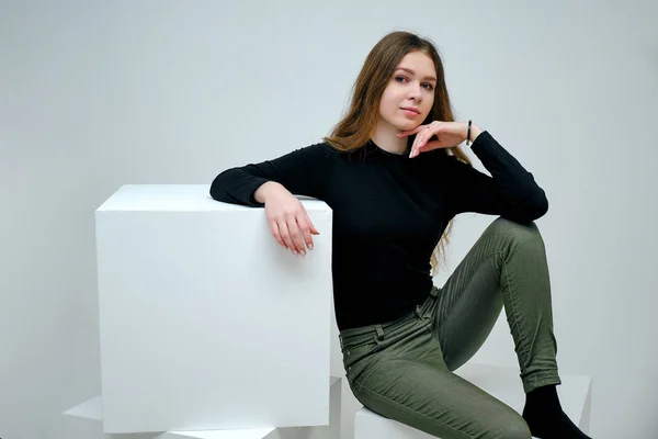 Concept Portrait of a pleasant friendly and optimistic happy young girl brunette in a black t-shirt smiling on a white background. Beautiful business woman showing copy space over white cube.