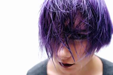 Bir gri t-shirt ve makyaj çerçevenin ortasında beyaz bir arka plan üzerinde ıslak, mor ve kısa saçlı oturan bir kız. O tepeden bakıyor ve kafası çalışmıyor.