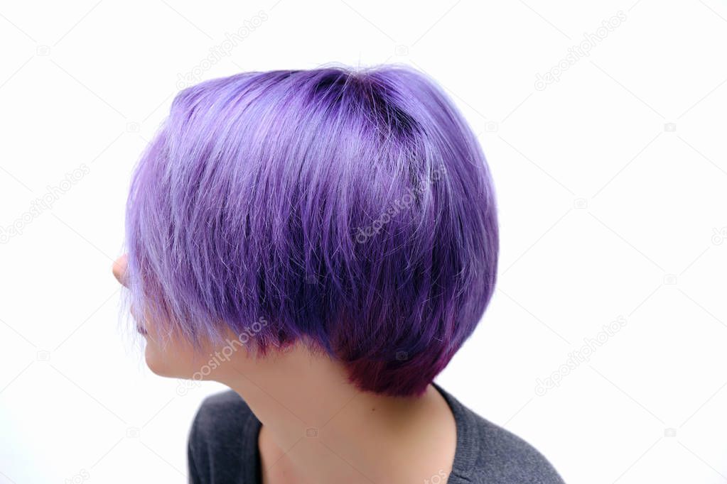 A girl in a gray t-shirt and makeup sitting with wet, purple and short hair on a white background in the middle of the frame. She looks down and her head is down.