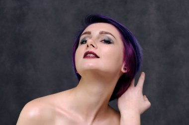 Mor saç ve kısa saç kesimi güzel, seksi bir kızla ortasında fotoğraf gri bir arka plan ve palyaçoluk ile oturuyor. Çıplak ve görünür omuz bir kız.