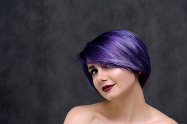 Mor saç ve kısa saç kesimi güzel, seksi bir kızla ortasında fotoğraf gri bir arka plan ve palyaçoluk ile oturuyor. Çıplak ve görünür omuz bir kız.