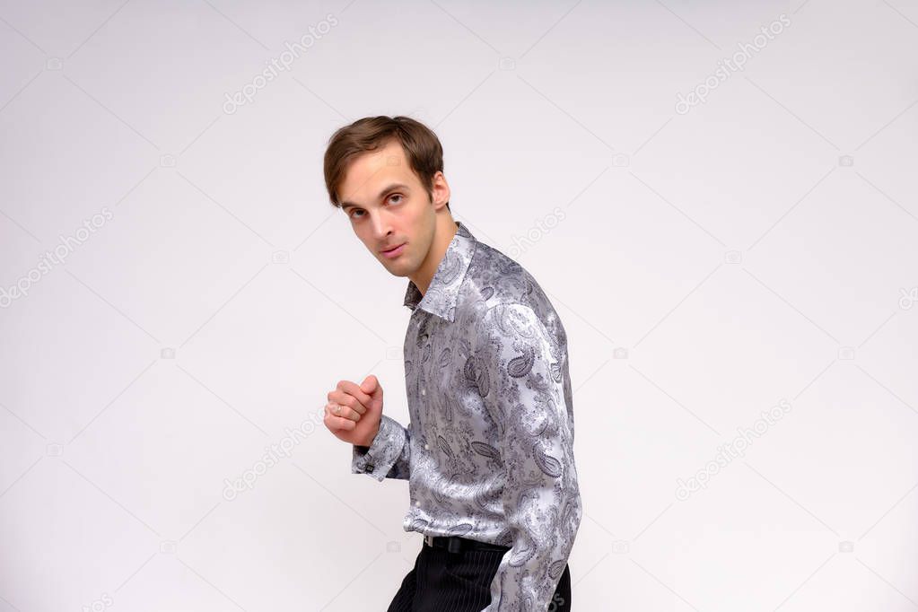 Concept studio portrait of a handsome young man isolated on a white background with different emotions in a silver-colored shirt. He stands directly in front of the camera in various poses.
