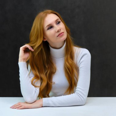 Kavramı Studio masada oturan gri bir arka plan üzerinde konuşmak güzel güzel kızıl saçlı kız portresi. O beyaz bir kazak giyiyor ve farklı duygular içinde farklı pozlar gösterir.