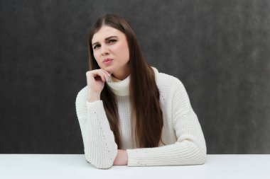 Kavramı Studio masada oturan gri bir arka plan üzerinde konuşurken bir çok güzel esmer kız portresi. O beyaz bir kazak giyiyor ve farklı duygular içinde farklı pozlar gösterir.