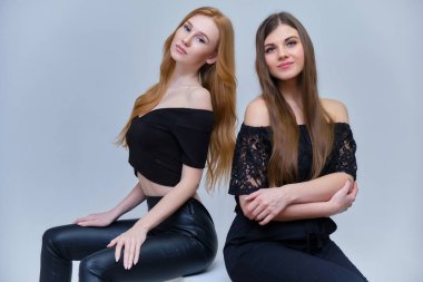 Kavramı Studio küpleri kamera önünde oturan gri bir arka plan üzerinde konuşurken iki sevimli güzel kız portresi. Farklı pozlar farklı duygular gösteriyorlar.
