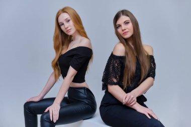 Kavramı Studio küpleri kamera önünde oturan gri bir arka plan üzerinde konuşurken iki sevimli güzel kız portresi. Farklı pozlar farklı duygular gösteriyorlar.