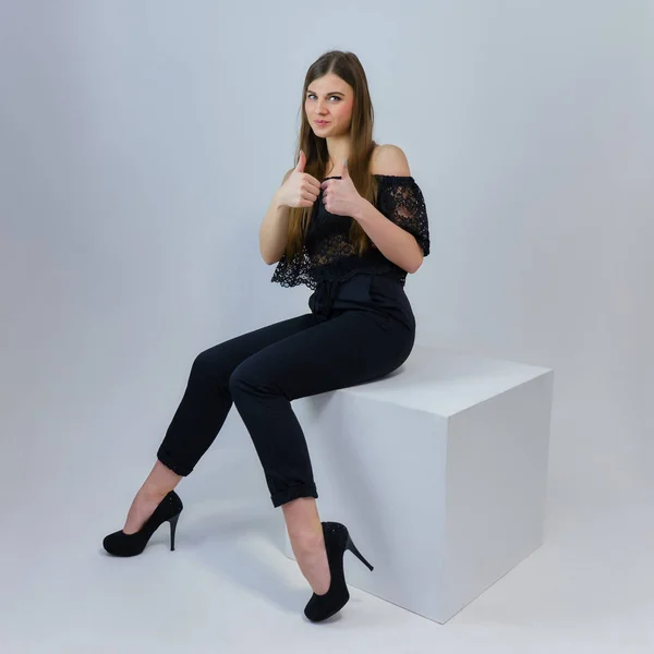 Concept portrait of a pretty beautiful brunette girl talking on a gray background in the studio sitting on a cube in front of the camera. They show different emotions in different poses.