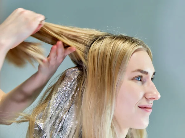 Konzeptarbeit einer Kosmetikerin im Büro. macht Haare, trägt Make-up auf grauem Hintergrund auf. — Stockfoto