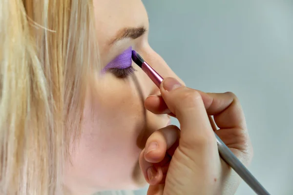 Konzeptarbeit einer Kosmetikerin im Büro. macht Haare, trägt Make-up auf grauem Hintergrund auf. — Stockfoto