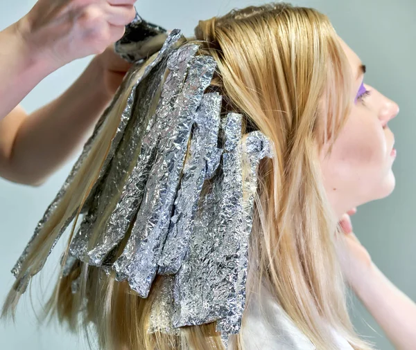 Konzeptarbeit einer Kosmetikerin im Büro. macht Haare, trägt Make-up auf grauem Hintergrund auf. — Stockfoto