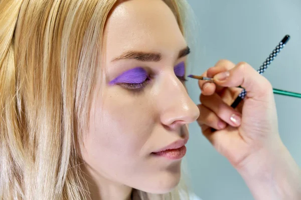 Begreppet arbete av en kosmetolog kosmetolog in med office. Gör håret, applicerar makeup på en grå bakgrund. — Stockfoto