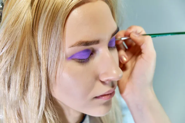 Trabajo conceptual de un cosmetólogo esteticista con oficina. Hace el pelo, aplica maquillaje sobre un fondo gris . — Foto de Stock