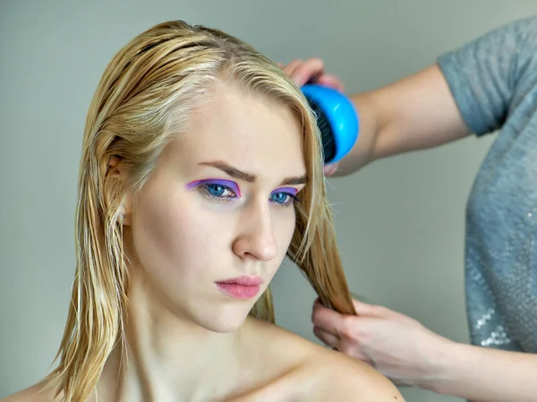 Begreppet arbete av en kosmetolog kosmetolog in med office. Gör håret, applicerar makeup på en grå bakgrund. — Stockfoto