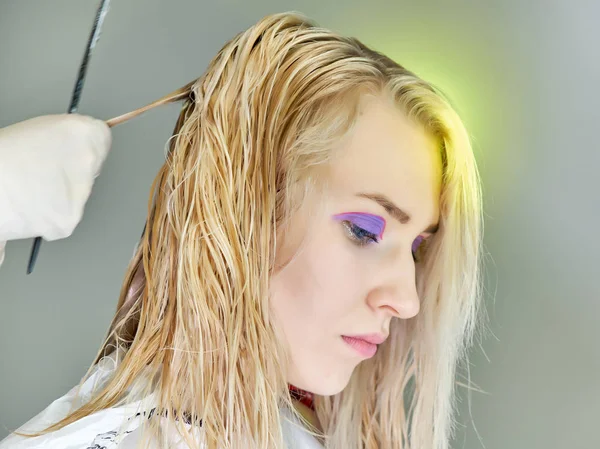 Konzeptarbeit einer Kosmetikerin im Büro. macht Haare, trägt Make-up auf grauem Hintergrund auf. — Stockfoto