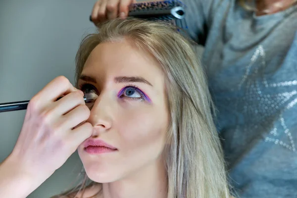 Konzeptarbeit einer Kosmetikerin im Büro. macht Haare, trägt Make-up auf grauem Hintergrund auf. — Stockfoto