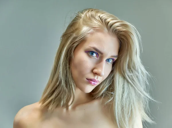 Closeup portrait concept of a beautiful blonde girl on a gray background. Hair develops in different directions. — Stock Photo, Image
