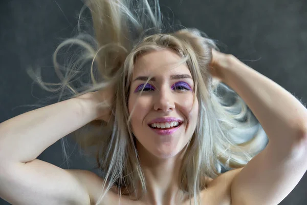 Nahaufnahme Portraitkonzept eines schönen blonden Mädchens auf grauem Hintergrund. Haare entwickeln sich in verschiedene Richtungen. — Stockfoto