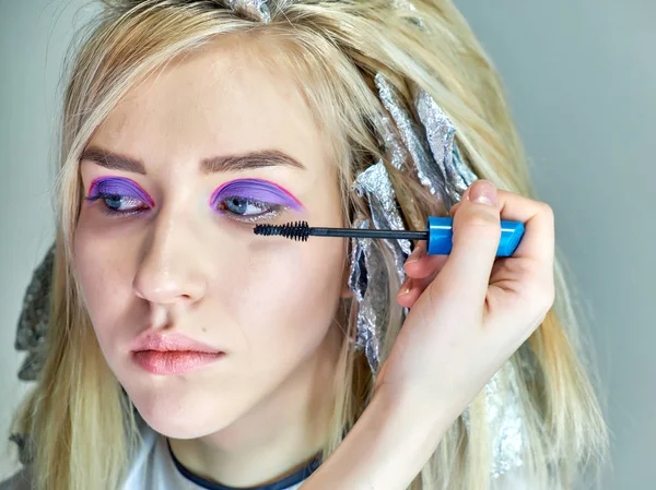 Concept work of a beautician cosmetologist in with office. Makes hair, applies makeup on a gray background. — Stock Photo, Image